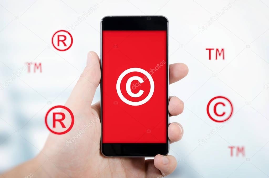 Copyright, trademark symbols flying around smartphone.