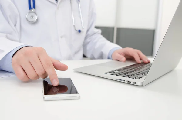 Доктор, який працює з телефоном і ноутбуком у лікарні або клініці — стокове фото