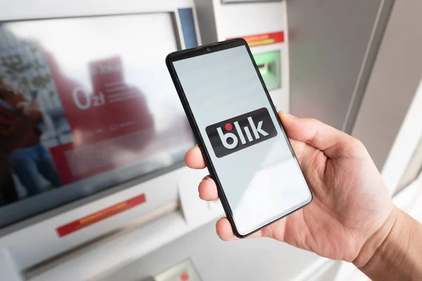 Hombre sosteniendo teléfono inteligente con el logotipo de Blik cerca de ATM —  Fotos de Stock
