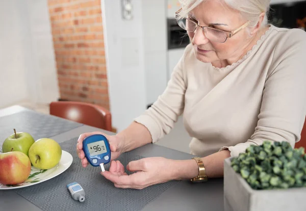 Starsza kobieta sprawdza poziom cukru we krwi w domu — Zdjęcie stockowe
