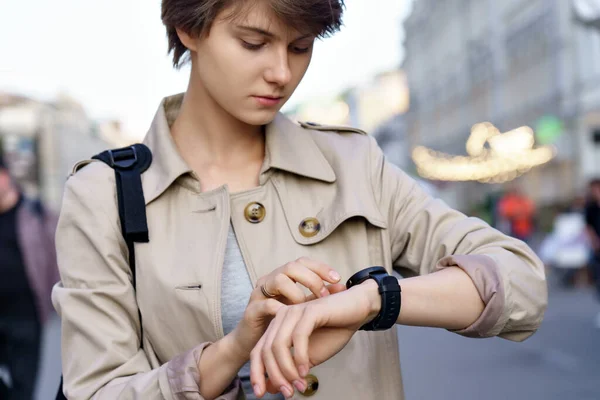 Teen girl using smart watch walking on city street.