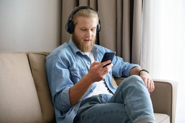 Young man wearing headphones using phone looking at screen at home.