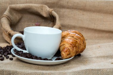 Kruvasan ve masanın üzerine fasulye ile kahve fincanı