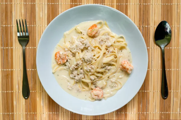Spagetti beyaz soslu karides ve hasır plat üzerinde kıyılmış domuz