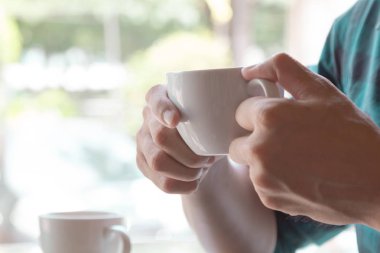 Sıcak latte fincan kahve onun elinde tutan işadamı; pencere Kafe'nin kopya alanı ile ışık