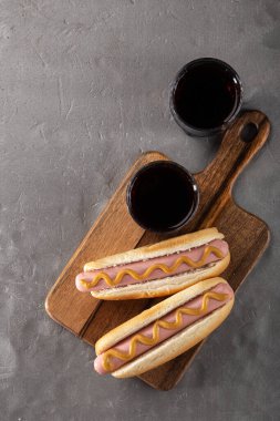 Tahtada hardallı sosisli sandviç. Sosisli sandviçler taş bir masada kola ile servis edilir. Metin için boş alan