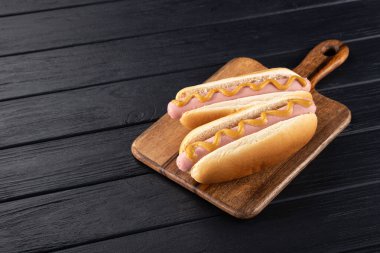 Tahtada hardallı sosisli sandviç. Sosisli sandviçler siyah masada servis edilir. Metin için boş alan