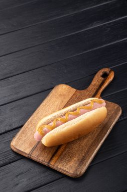 Tahtada hardallı sosisli sandviç. Sosisli sandviçler siyah masada servis edilir. Metin için boş alan