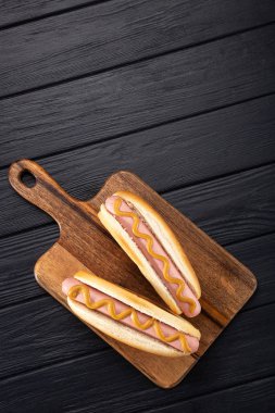 Tahtada hardallı sosisli sandviç. Sosisli sandviçler siyah masada servis edilir. Metin için boş alan