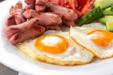 Ev yapımı nefis kahvaltı, güneşli tarafı kızarmış yumurta, sosis, sebze, reçel, taş bir masada sade kahve. Çiçekler ve beyaz tabaklarla servis edilen kahvaltı.