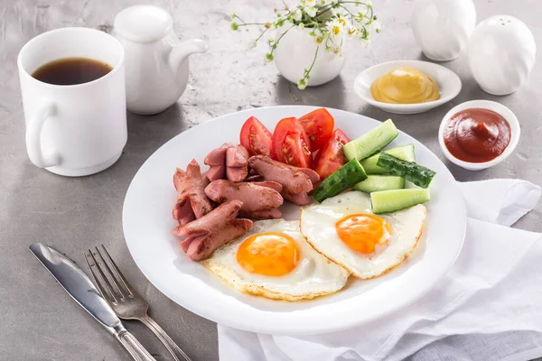 Homemade delicious breakfast with sunny side up fried egg, sausage, vegetable, jam, black coffee on a stone table. Breakfast served with flowers and white dishes