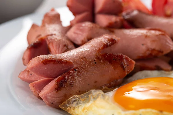 Homemade delicious breakfast with sunny side up fried egg, sausage, vegetable, jam, black coffee on a stone table. Breakfast served with flowers and white dishes