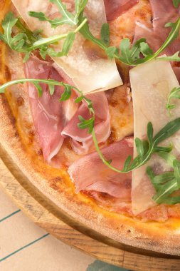 Masada taze pizza var. Prosciutto (parma jambonlu), roket salatası (roket) ve parmesanlı pizza, akşam yemeği için ahşap bir masada servis edilir. İtalyan mutfağı. 