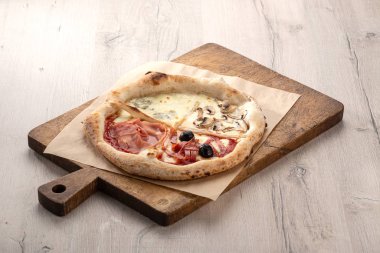 Masada taze pizza var. Dört mevsim pizza. Taze İtalyan Four Seasons Pizza (Pizza Quattro Stagioni) mutfak masasının üzerinde. Akşam yemeği için ahşap masada ev yapımı lezzetli İtalyan pizzası. İtalyan mutfağı.