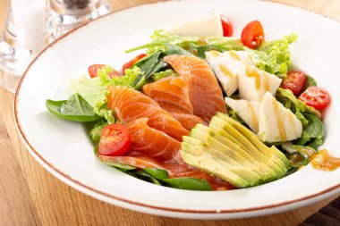 Lezzetli taze salata. Somonlu salata, avokado, marul, domates, parmesan, peynir, ıspanak. Avokado ve sebzeli taze somon salatası. Salata 'nın görüntüsünü kapat