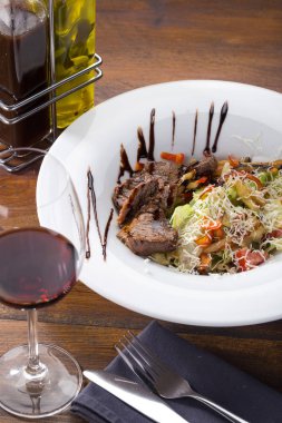 Lezzetli taze salata. Dana etli salata, domates, biber, ahşap zemin üzerinde şarap ile servis edilen marul. Restoran yemekleri, kapatın. Et salatası. Salatayı sıcak dana etiyle kapatın..