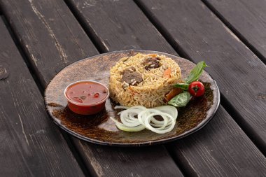 Tahta bir masanın üzerinde, dökme demir bir tavada eti olan Özbek pilavı. Geleneksel Asya yemeği - pilav bir tabakta pirinç, sebze ve et