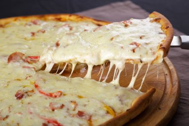 Köy ahşap bir masada erimiş peynirli sıcak bir dilim pizza. Lezzetli. Domuz pastırmalı, sosisli, salamlı, pepperonili ve zeytinli büyük etli pizza..
