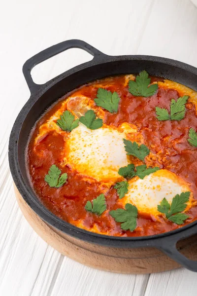 Shakshuka - domates sosunda kızartılmış yumurta, acı biber, soğan ve baharat. Shakshuka çırpılmış yumurta, beyaz ahşap arka planda domates ve sebze. Kızartma Tavasında Kahvaltı.