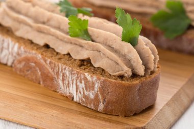 Beyaz bir masada etli börek var. Beyaz masa üzerinde ciğer ezmesi ve bitkilerle Kanepe mini sandviç.