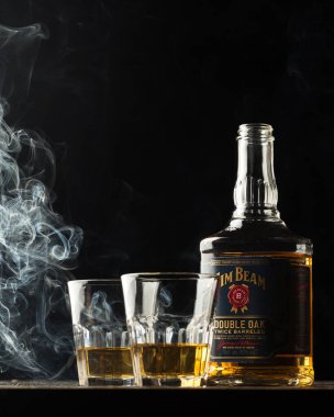 Jim Beam en çok satan burbon markalarından biridir. Dumanlı alkol. Jim Beam şişe siyah arka planda gözlük ile düzenlenmiş.