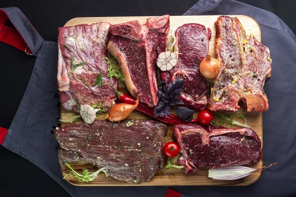 different types of meat on the board. Different types of Raw fresh meat Steaks and meat cleaver on cutting board. Assorted raw meat. Rib eye steak on the bone, veal shank (ossobuco), fillet