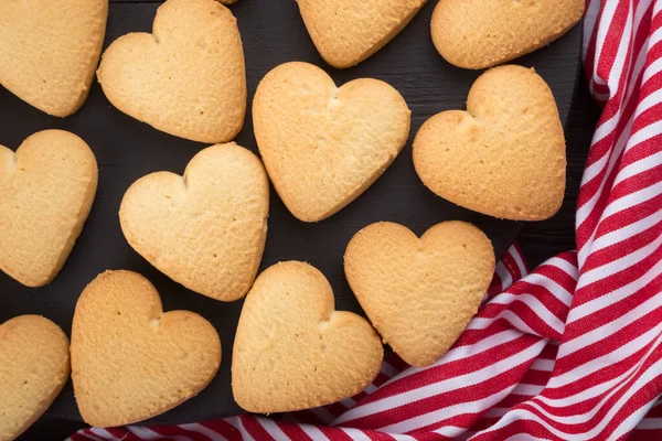 Heart shaped cookies decorated for Valentine\'s Day. Free space for text. Two heart shaped cookies with jam on a black wooden table. Wooden plate with heart shaped cookies on a black wooden table. Like postcard. Background with cookies