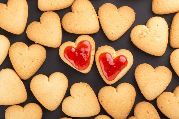 Heart shaped cookies decorated for Valentine\'s Day. Free space for text. Two heart shaped cookies with jam on a black wooden table. Wooden plate with heart shaped cookies on a black wooden table. Like postcard