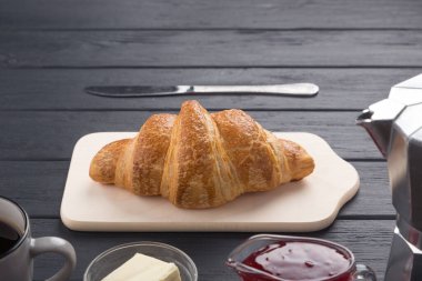 Siyah ahşap bir masada taze kruvasanlar. Kahve, kahve demliği, tereyağı, reçel ve mavi peçeteyle servis edilir. Taze Fransız kruvasanı. Sıcak taze tereyağlı rulo. Kahvaltıda. Metin için boş alan. 