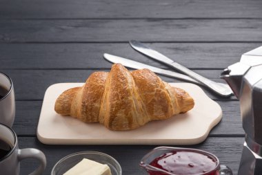 Siyah ahşap bir masada taze kruvasanlar. Kahve, kahve demliği, tereyağı, reçel ve mavi peçeteyle servis edilir. Taze Fransız kruvasanı. Sıcak taze tereyağlı rulo. Kahvaltıda. Metin için boş alan. 