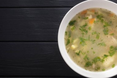 Bir kase tavuk çorbası. Siyah ahşap bir masada beyaz tabakta tavuk çorbası. Tavuklu erişte. Bakso, erişteli köfte çorbası. Metin için boş alan. Yukarıdan bak. Üst görünüm. 