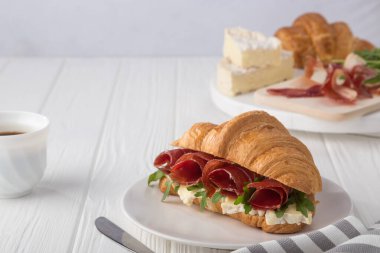 Beyaz ahşap masada jambon, peynir ve roka ile taze kruvasan sandviçi. Kruvasan kahvaltısı. Taze Fransız kruvasanı. Metin için boş alan. Yukarıdan bak. Üst görünüm.