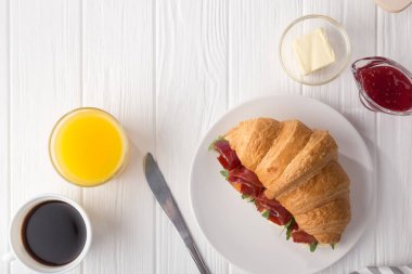 Beyaz ahşap masada jambon, peynir ve roka ile taze kruvasan sandviçi. Kahve, peynir, jambon, portakal suyu ve reçelle servis edilir. Taze Fransız kruvasanı. Metin için boş alan. Yukarıdan bak. Üst görünüm.