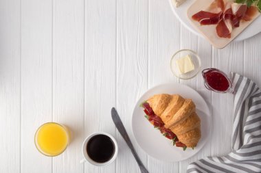Beyaz ahşap masada jambon, peynir ve roka ile taze kruvasan sandviçi. Kahve, peynir, jambon, portakal suyu ve reçelle servis edilir. Taze Fransız kruvasanı. Metin için boş alan. Yukarıdan bak. Üst görünüm.