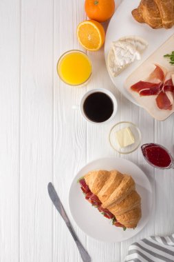 Beyaz ahşap masada jambon, peynir ve roka ile taze kruvasan sandviçi. Kahve, peynir, jambon, portakal suyu ve reçelle servis edilir. Taze Fransız kruvasanı. Metin için boş alan. Yukarıdan bak. Üst görünüm.