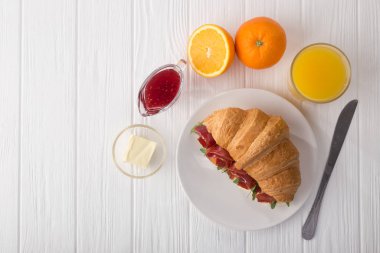 Beyaz ahşap masada jambon, peynir ve roka ile taze kruvasan sandviçi. Kahve, peynir, jambon, portakal suyu ve reçelle servis edilir. Taze Fransız kruvasanı. Metin için boş alan. Yukarıdan bak. Üst görünüm.