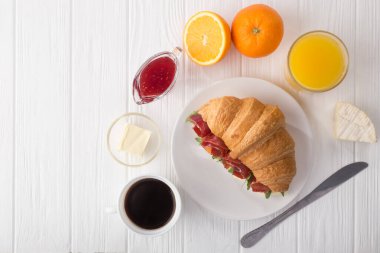 Beyaz ahşap masada jambon, peynir ve roka ile taze kruvasan sandviçi. Kahve, peynir, jambon, portakal suyu ve reçelle servis edilir. Taze Fransız kruvasanı. Metin için boş alan. Yukarıdan bak. Üst görünüm.