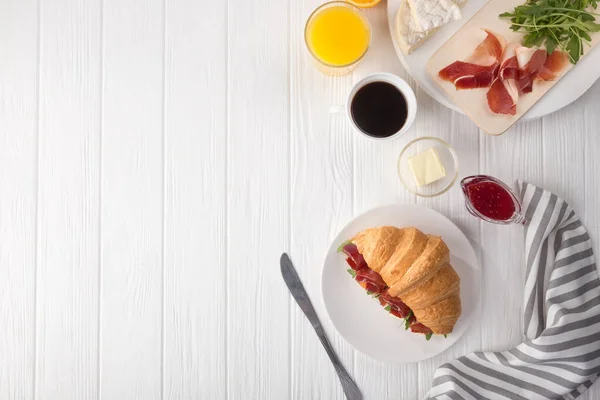 Fresh croissant sandwich with ham, cheese and arugula on white wooden table. Served with Coffee, cheese, ham, orange juice, jam. Fresh French Baked Croissants. Free space for text. View from above. Top view.