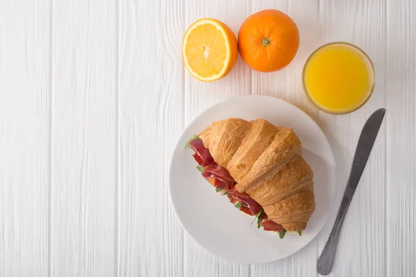 Fresh croissant sandwich with ham, cheese and arugula on white wooden table. Served with Coffee, cheese, ham, orange juice, jam. Fresh French Baked Croissants. Free space for text. View from above. Top view.