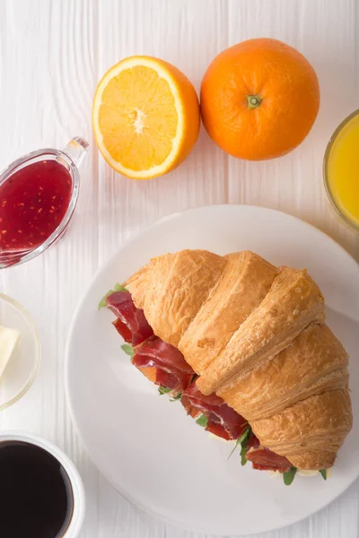 Fresh croissant sandwich with ham, cheese and arugula on white wooden table. Served with Coffee, cheese, ham, orange juice, jam. Fresh French Baked Croissants. Free space for text. View from above. Top view.