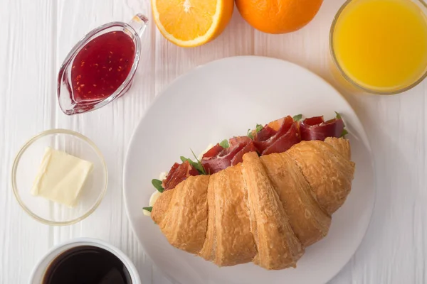 Fresh croissant sandwich with ham, cheese and arugula on white wooden table. Served with Coffee, cheese, ham, orange juice, jam. Fresh French Baked Croissants. Free space for text. View from above. Top view.