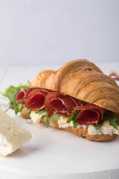 Fresh croissant sandwich with ham, cheese and arugula on white wooden table. Served with Coffee, cheese, ham, orange juice, jam. Fresh French Baked Croissants. Free space for text.