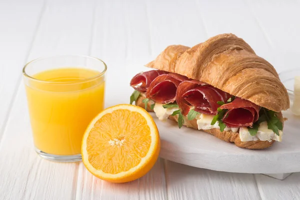 Fresh croissant sandwich with ham, cheese and arugula on white wooden table. Served with Coffee, cheese, ham, orange juice, jam. Fresh French Baked Croissants. Free space for text.