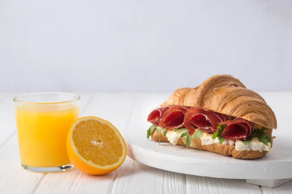 Fresh croissant sandwich with ham, cheese and arugula on white wooden table. Served with Coffee, cheese, ham, orange juice, jam. Fresh French Baked Croissants. Free space for text.