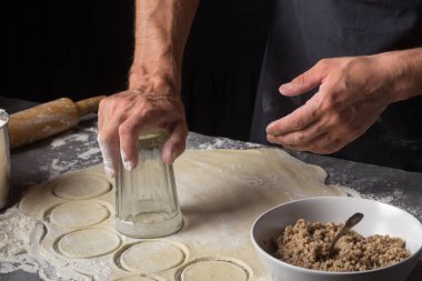 Bir adam et, soğan ve pastırma ile Varenyky ya da hamur tatlısı için para kazanıyor. Yüzü olmayan siyah önlüklü bir adam. Adam hamur çemberlerini bir bardakla sıkıyor. Pastacı Stone 'un yakın plan fotoğrafında erkek eli ile para kazanıyor.