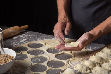 Bir adam et, soğan ve pastırma ile varenikli ya da hamur tatlısı yapıyor. Adam hamuru etle dolduruyor. Yüzü olmayan siyah önlüklü bir adam. Pastacı Stone 'un yakın plan fotoğrafında erkek eli ile para kazanıyor.  