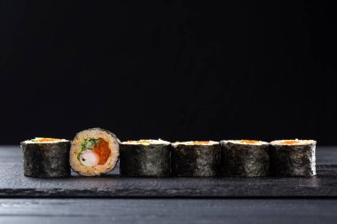 Karanlık bir arka planda karidesli suşi rulosu. Karidesli geleneksel Japon dürümü. Suşi taştan bir tabakta ve koyu betondan bir arka planda. Suşi seti ve yemek çubukları. Taze Japon mutfağı. Asya yemeği. Menü için suşi resmi. Kapat.