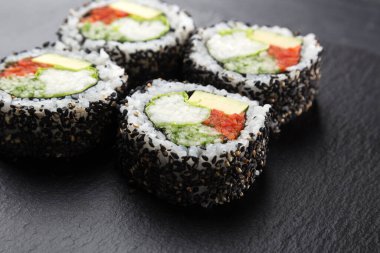 Sebzeli suşi dürümü ve karanlık bir arka plan. Suşi taştan bir tabakta ve koyu betondan bir arka planda. Suşi seti ve yemek çubukları. Taze Japon mutfağı. Asya yemeği. Menü için suşi resmi. Kapat.