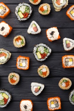 Suşi seti. Maski, gunkan ve suşi ruloları taş levhada servis edilir. Suşi taştan bir tabakta ve koyu betondan bir arka planda. Suşi seti ve yemek çubukları. Taze Japon mutfağı. Asya yemeği. Menü için suşi resmi. Kapat.