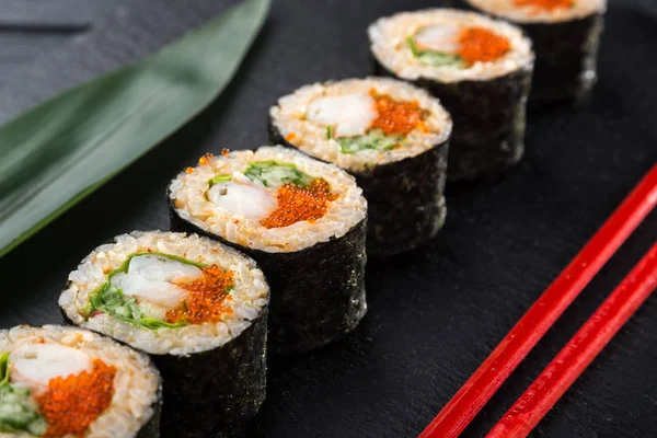 Sushi Rolls with shrimp on a dark background. Japanese traditional roll with prawn. Sushi set on a stone plate and dark concrete background. Sushi roll set and chopsticks. Fresh Japanese cuisine. asian food. Sushi image for menu. close up